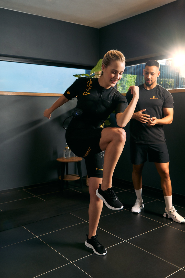 Personal trainer guiding a client in a SYMBIONT EMS suit during a trial session at a local EMS studio. Experience personalized training, guidance, and motivation in your EMS trial.